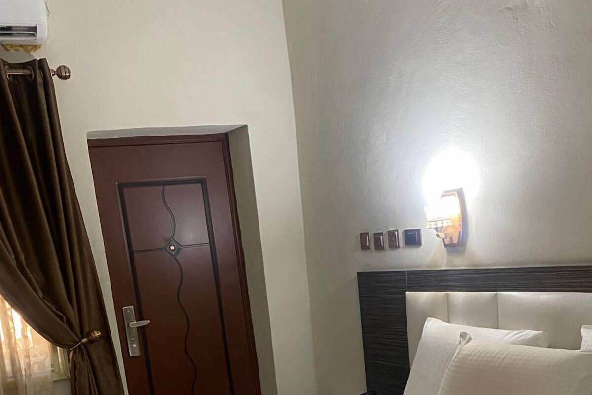 A hotel room with a large bed, a wooden door, and a wall-mounted light fixture.