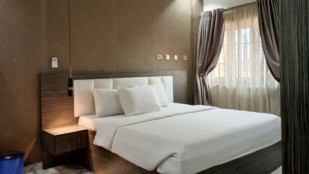 Une chambre d’hôtel moderne avec un grand lit, une table de chevet et une petite poubelle.