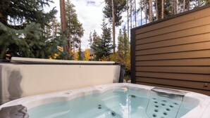 A hot tub in an outdoor setting with a wooden deck and tall trees in the background.