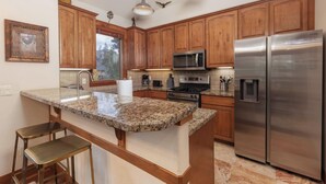 A kitchen with wooden cabinets, granite countertops, stainless steel appliances, and pendant lighting.