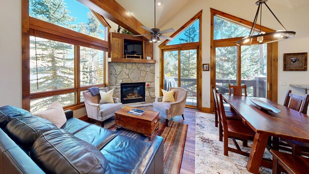 A spacious living area with a fireplace, large windows, a ceiling fan, and a dining table.