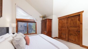 A bedroom with a large bed, wooden wardrobe, and a window with curtains.