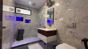 A modern bathroom with a marble wall, a glass shower enclosure, a white sink with a wooden countertop, and a large mirror.