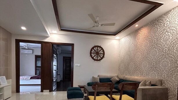 A modern living room with a sofa, chairs, a ceiling fan, and a decorative wall piece. - HomiStay (Panchkula)
