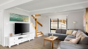 A modern living room with a flat-screen TV, a gray sofa, a wooden coffee table, and a staircase with wooden railings. - OPI San Remo with water views (San Remo)