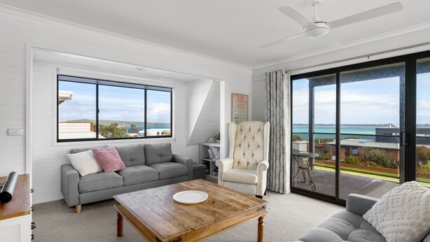 A spacious living room with a grey sofa, a wooden coffee table, and a white armchair. A large window offers a view of the sea and buildings. - OPI San Remo with water views (San Remo)