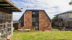 A modern brick house with a sloped roof, a visible garage door, and a small front yard with a lawn and a wooden fence. - OPI San Remo with water views (San Remo)
