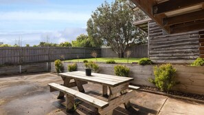 A wooden picnic table with benches in a backyard with a wooden fence and small bushes. - OPI San Remo with water views (San Remo)