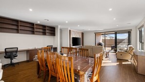 Un salon moderne comprenant un coin repas, des meubles en bois, un téléviseur à écran plat et une porte-fenêtre coulissante donnant sur une terrasse extérieure.
