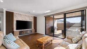 Un salon moderne doté d’un téléviseur à écran plat, de planchers en bois, d’une cheminée et d’une porte-fenêtre coulissante donnant sur une cour arrière avec un barbecue.