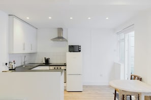 A modern kitchen with white cabinetry, a stainless steel range hood, a microwave, and a built-in oven. - Bright Studio Flat with Private Patio, Fulham (Greater London)