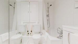 A modern bathroom with two toilets, a shower, and a bathtub.