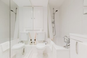 A modern bathroom with two toilets, a shower, and a bathtub.