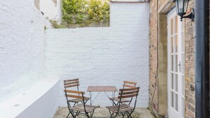 A small outdoor seating area with a white brick wall, a wooden table, and four wooden chairs.