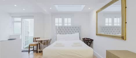 A modern bedroom with a large bed, a skylight, a mirror, and a view of the outdoors.