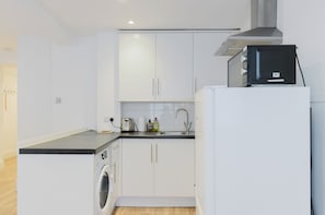 A compact kitchen with white cabinets, a built-in washing machine, a microwave, and a sink. - Bright Studio Flat with Private Patio, Fulham (Greater London)