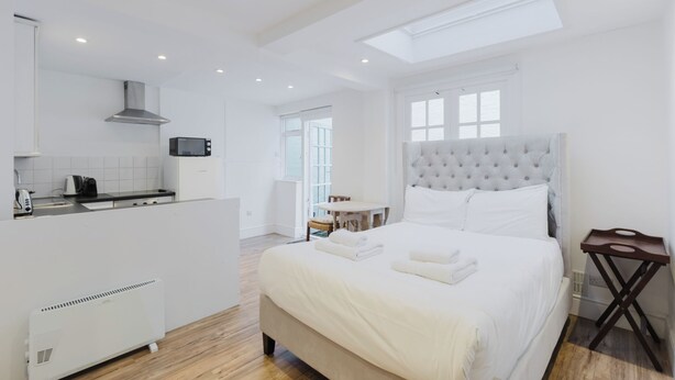 A modern bedroom with a large bed, a kitchenette, and a view of the outdoors.