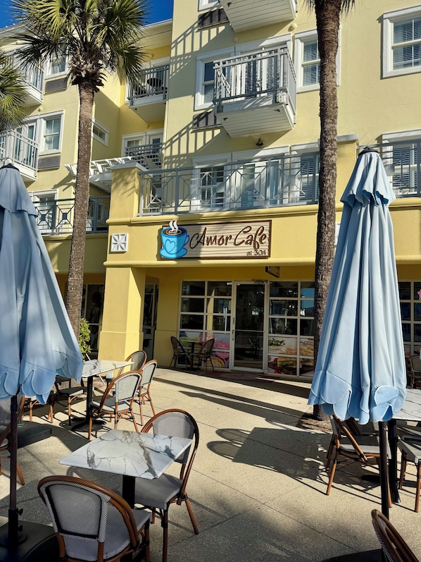 An outdoor seating area with tables and chairs, a café sign, and a building with balconies.