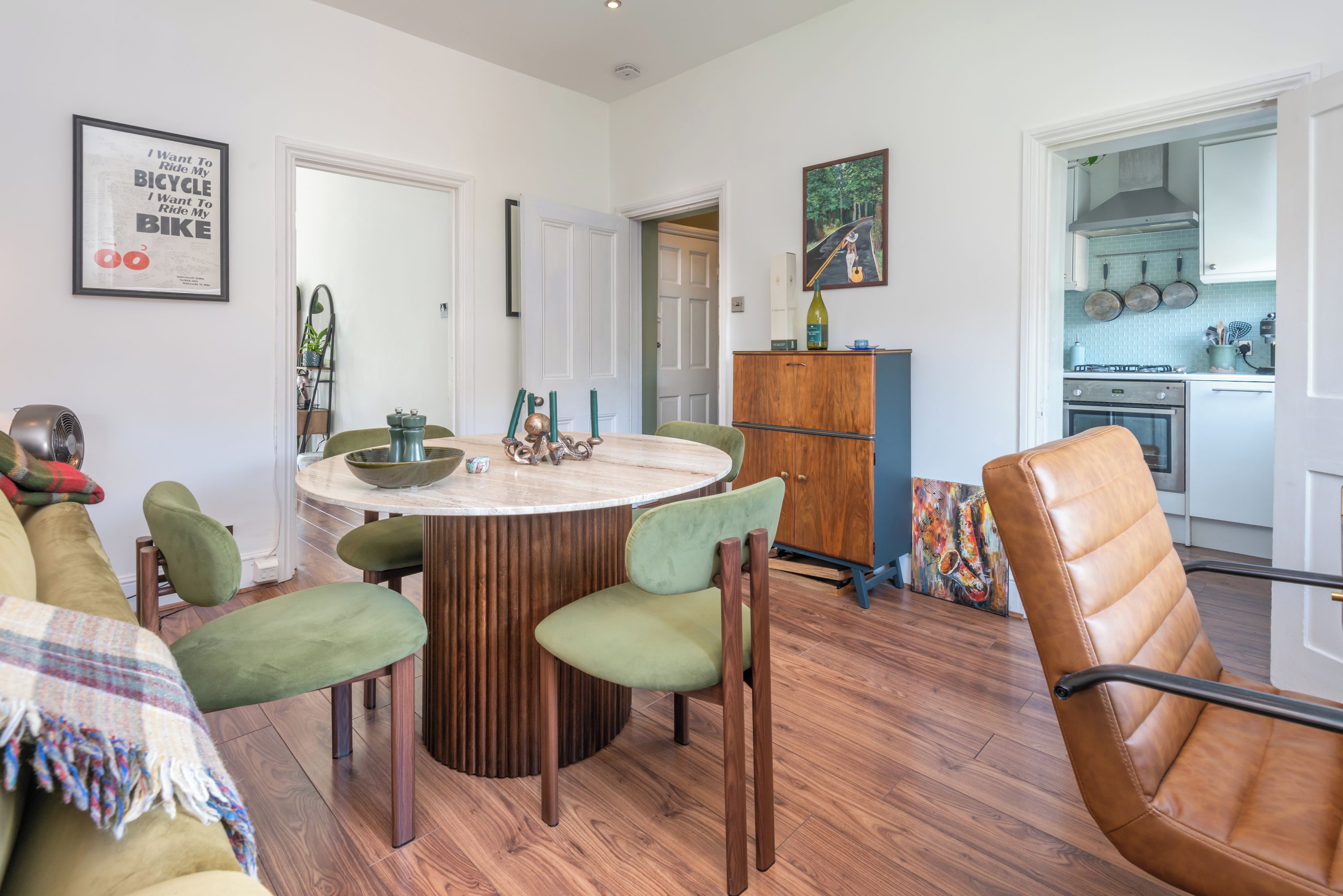 Un coin repas avec une table ronde, des chaises vertes et un buffet en bois.