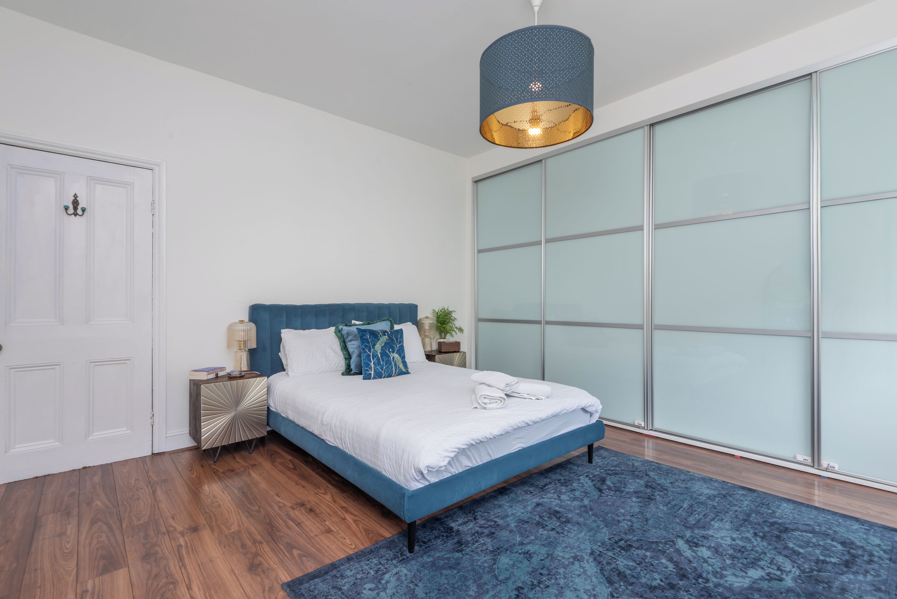 A bedroom with a bed, bedside table, lamp, and a large window.
