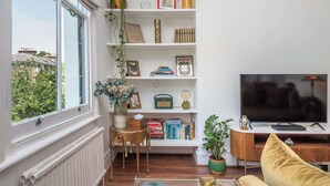 Un salon avec une grande fenêtre, une bibliothèque, un téléviseur et un canapé.