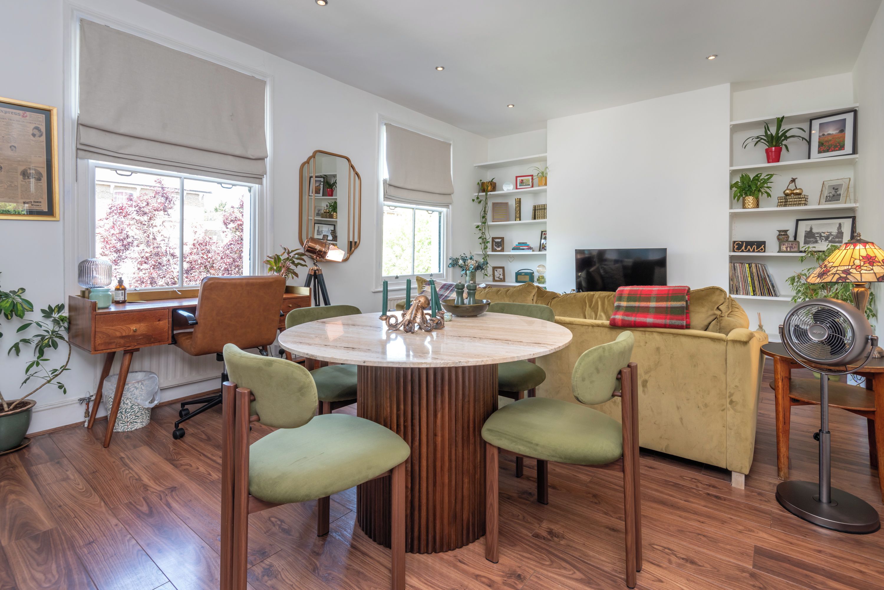 Een moderne woonkamer met een ronde houten tafel, groene stoelen, een gele bank en een televisie.