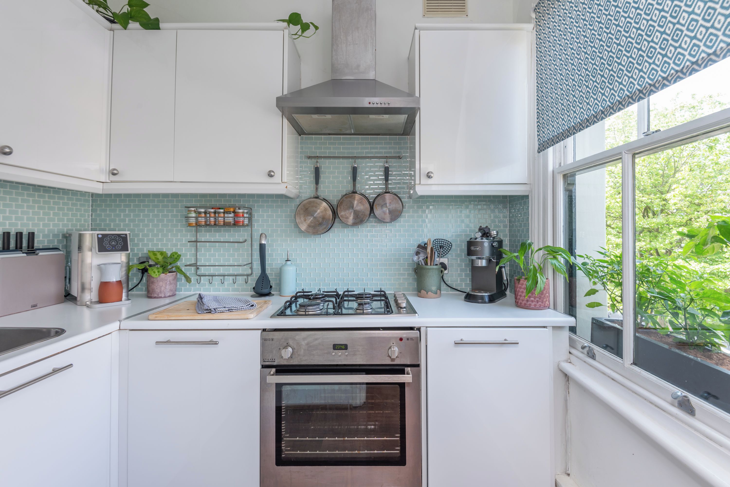 Una cocina moderna con armarios blancos, una estufa a gas, un horno y una ventana con vista a follaje.