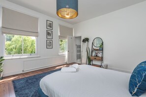 A bedroom with a large bed, a window, a radiator, a mirror, and a plant. - Modern 1BDR with Parking and Shared Garden (Greater London)