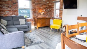 Een woonkamer met een grijze bank, een gele fauteuil en een houten eettafel.