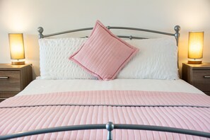 A neatly made bed with a pink quilt, white pillows, and two bedside lamps. - Bryn Bethel - sleeps 6 guests in 3 bedrooms (Caernarfon)
