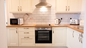 Een keuken met witte kastjes, een magnetron, oven, broodrooster en waterkoker.