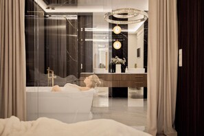 A modern bathroom with a bathtub, a vanity with a mirror, and a chandelier. - Jacuzzi Mirror Suite Granaria by Downtown Apartments (Gdańsk)
