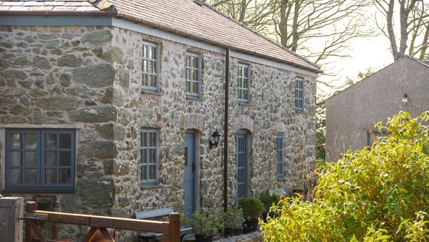 A stone building with multiple windows and a wooden fence in the foreground. - Y Wennol - sleeps 8 guests  in 3 bedrooms (Llangefni)