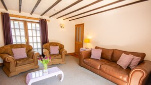 A living room with two brown leather sofas, a white coffee table, and a wooden door. - Y Wennol - sleeps 8 guests  in 3 bedrooms (Llangefni)