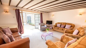 A cozy living room with a brown leather sofa, a patterned armchair, and a television on a stand. - Y Wennol - sleeps 8 guests  in 3 bedrooms (Llangefni)