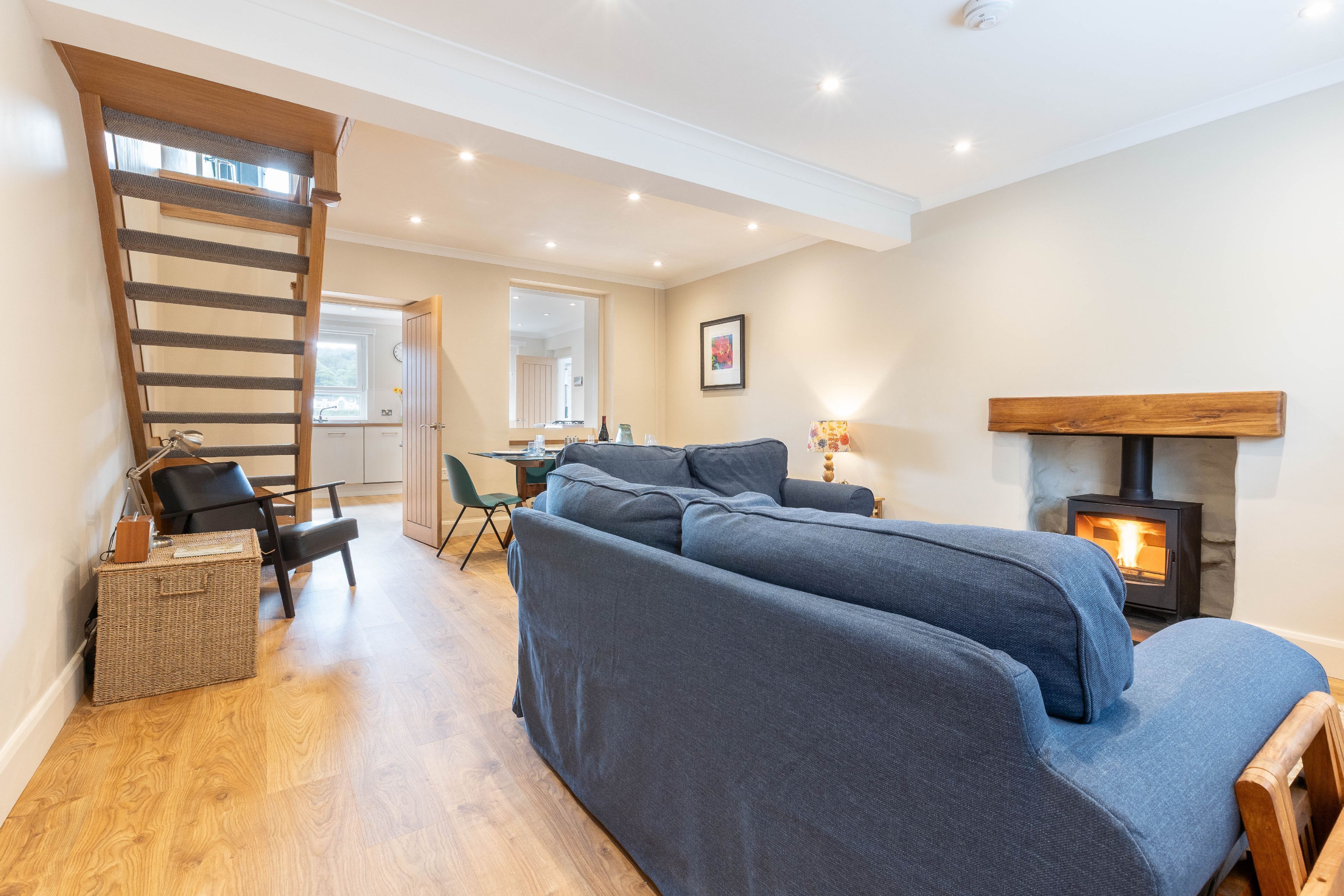 A modern living room with a sofa, a wooden staircase, a fireplace, and a dining area.