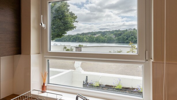 Habitació amb una finestra gran que dona a un llac i vegetació, un lavabo blanc i un armari de fusta.