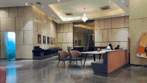 A modern lobby with a reception desk, seating area, and a large chandelier. - Luxury Stay Supernova (Noida)