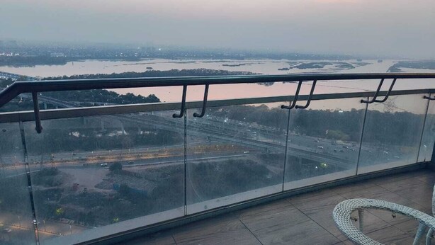 A balcony with a view of a cityscape and a river. There are two wicker chairs on the floor. - Luxury Stay Supernova (Noida)