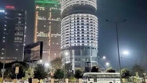 A tall, cylindrical building with a distinctive spiral design, illuminated with vertical stripes of red, green, and white lights. - Luxury Stay Supernova (Noida)