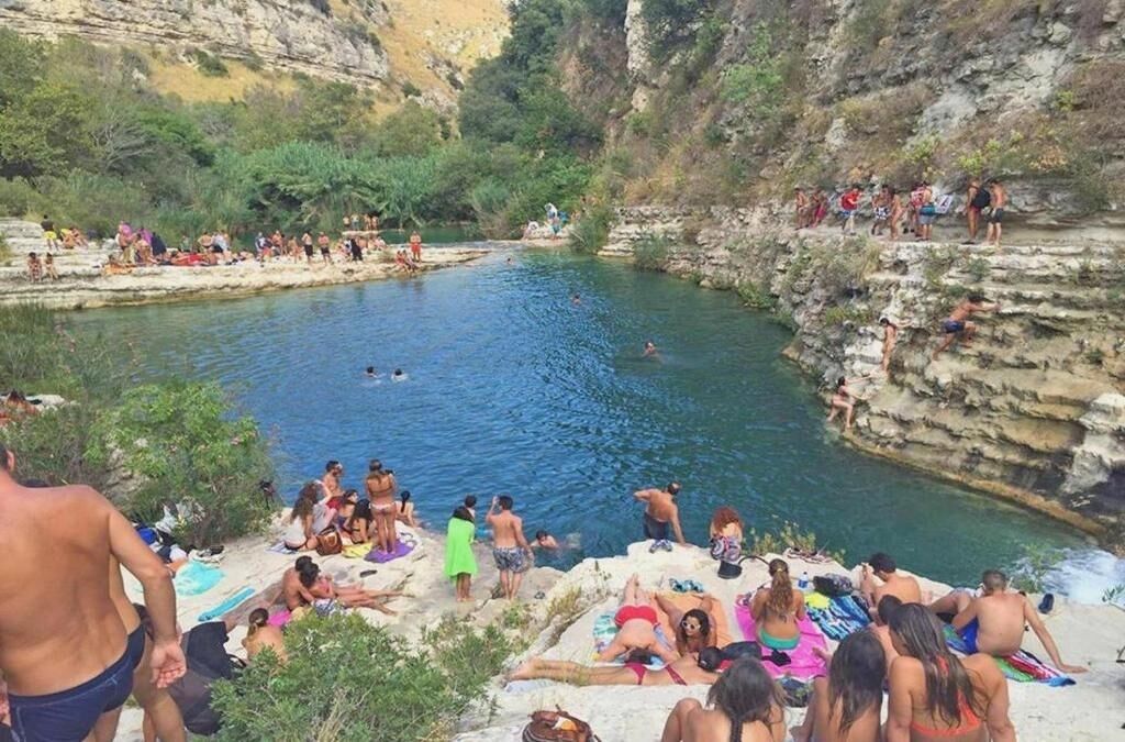 Ein natürlicher Pool, umgeben von steinigen Klippen, mit Menschen, die schwimmen und am Ufer entspannen.