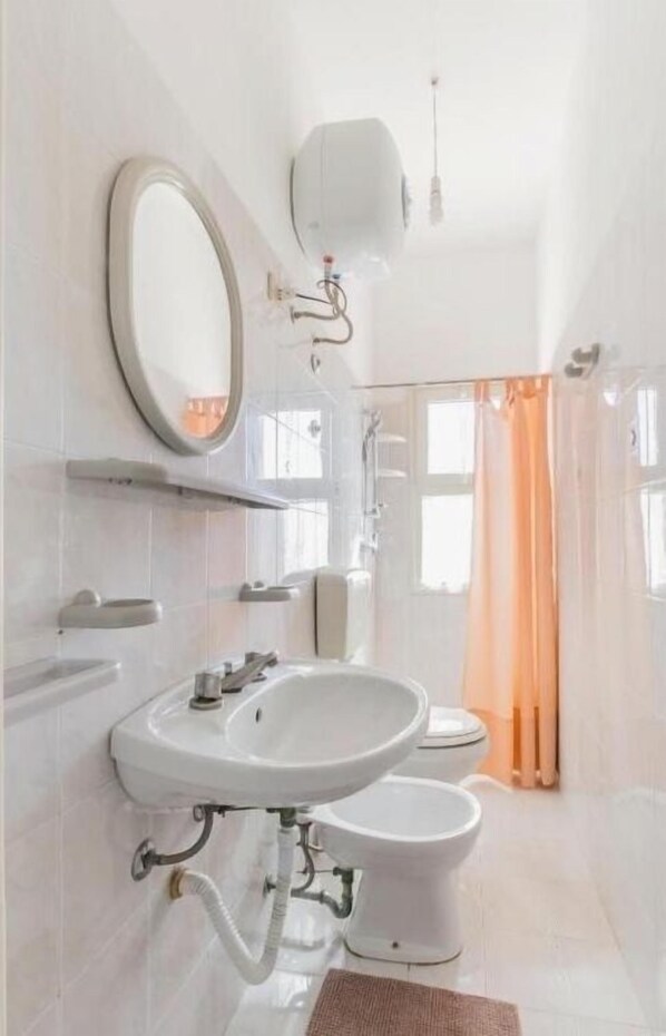 Un baño moderno con un lavabo blanco, un espejo y un inodoro. Hay una zona de ducha con puerta de cristal y cortina de ducha naranja.