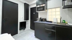 Una cocina moderna con armarios negros, una campana extractora de acero inoxidable, un microondas integrado y una ventana con persianas.