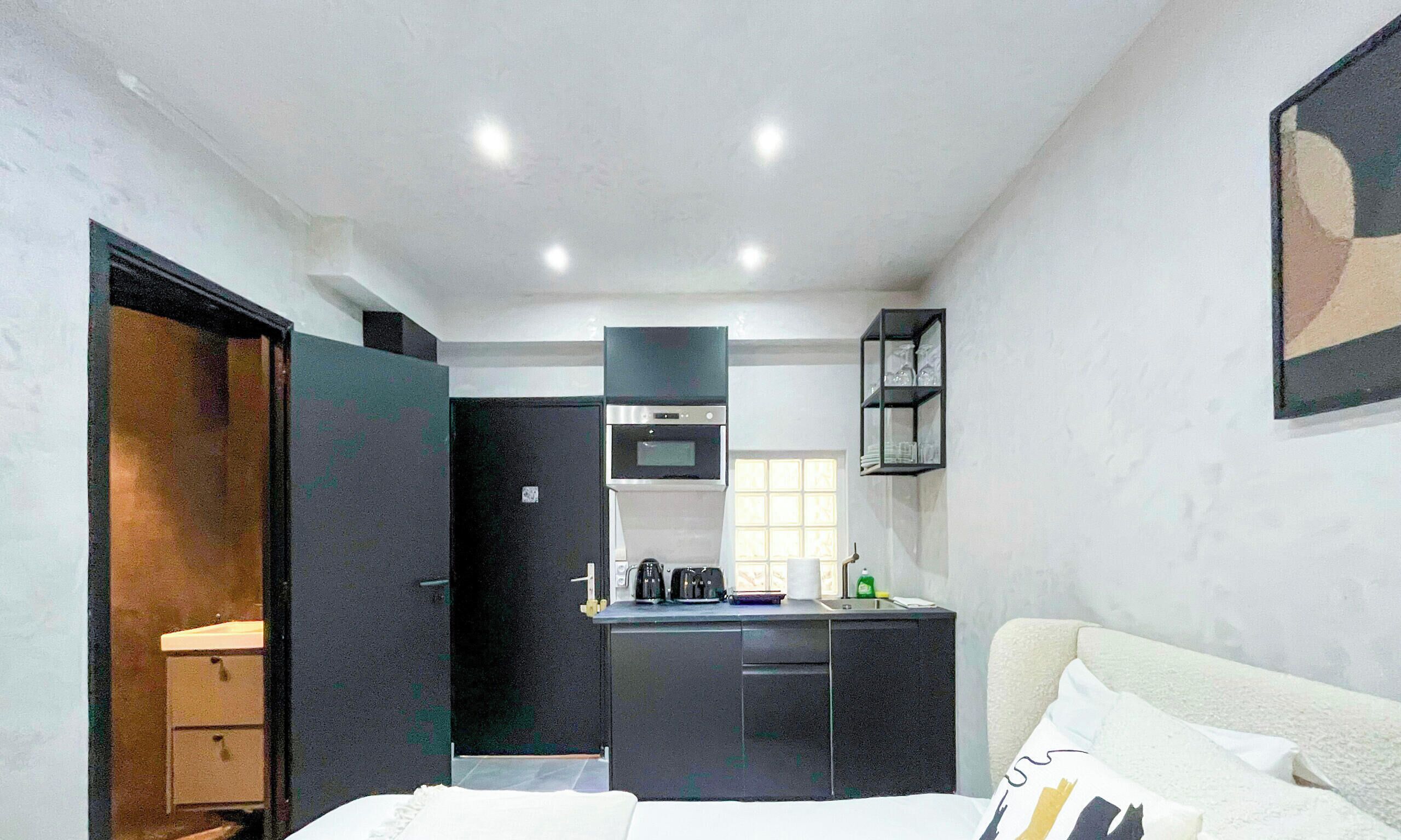 A compact hotel room with a bed, a desk, and a kitchenette.