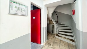 Un pasillo con una puerta roja, una escalera y un detector de incendios.