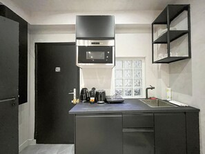A compact kitchen with a microwave, coffee maker, and kettle on the counter, a black door, and a window with decorative glass panels. - UrbanFlat 11 - Cosy king studio near champs Elysees (París)