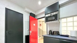 Una cocina compacta con microondas, cafetera y una puerta roja.