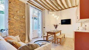 A cozy living room with a brick wall, a wooden ceiling, a dining area with a table and bench, and a kitchen with a red counter. - Superb air-conditioned apartment in the center of Paris/Le Marais (Paris)