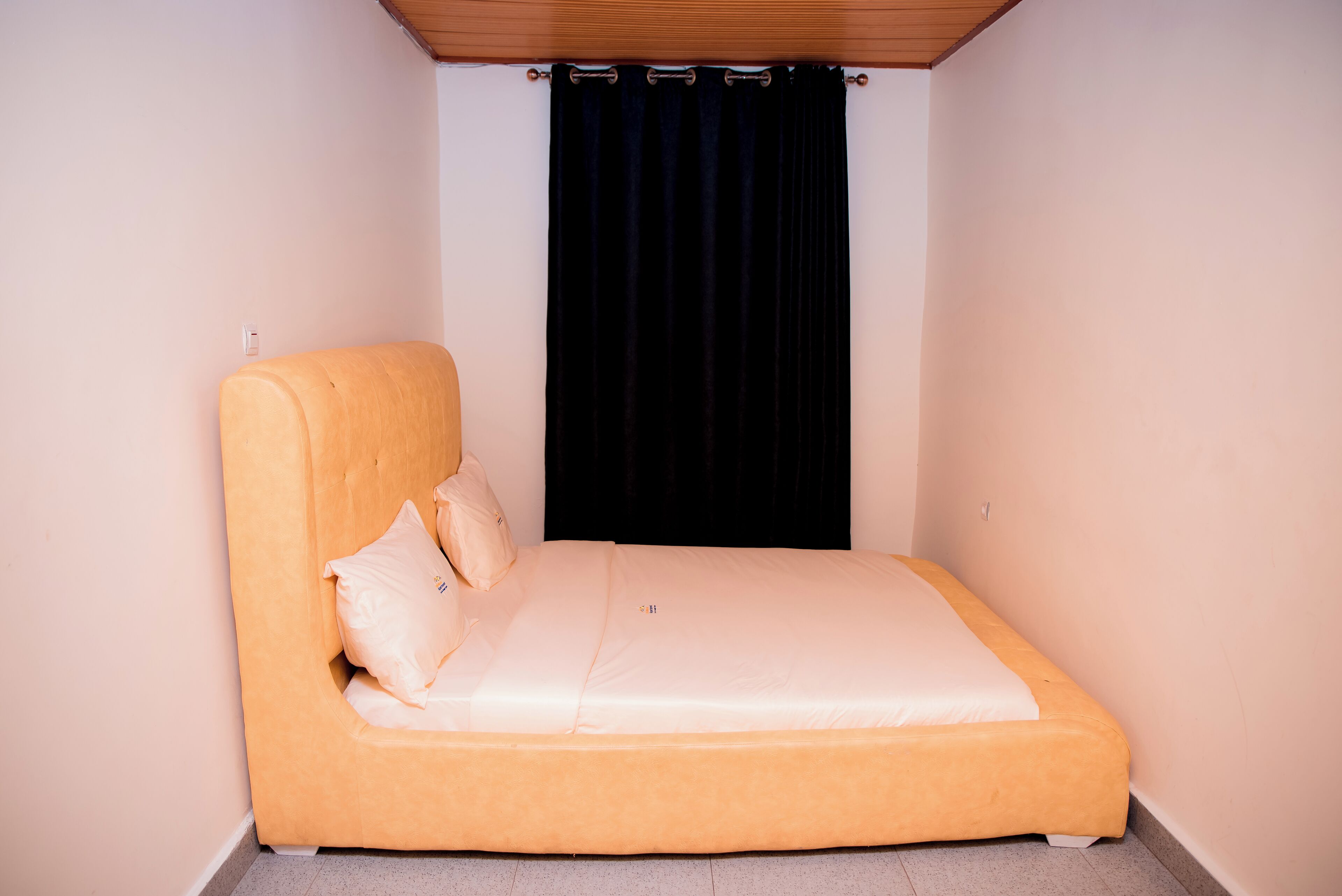 A single bed with a headboard, two pillows, and a black curtain.