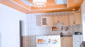 A kitchen with wooden cabinets, a chandelier, and patterned wallpaper. - The Moon Crib (Gisenyi)